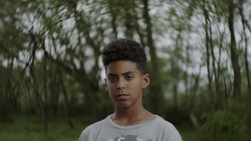 Boy stands near trees while looking sad