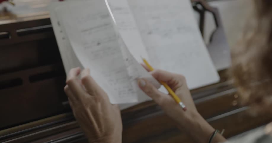 A woman reads from a notebook on a piano