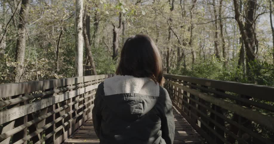 A woman walks over a wood bridge in the woods
