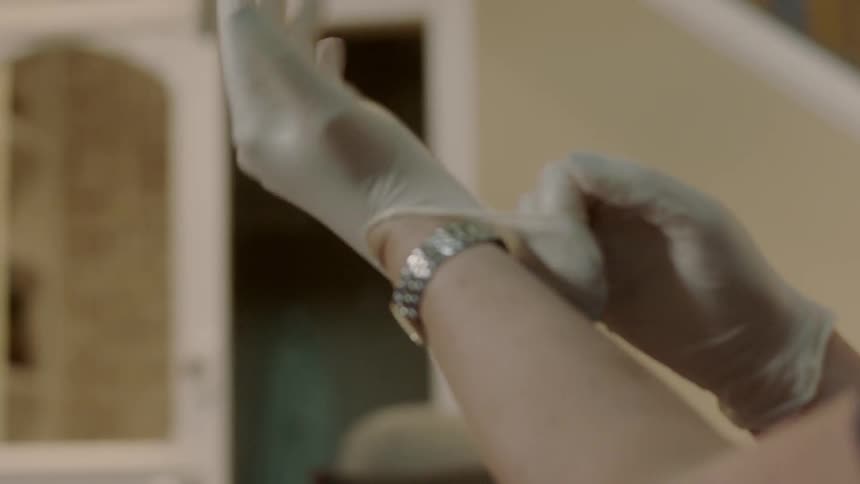A person puts on white rubber gloves