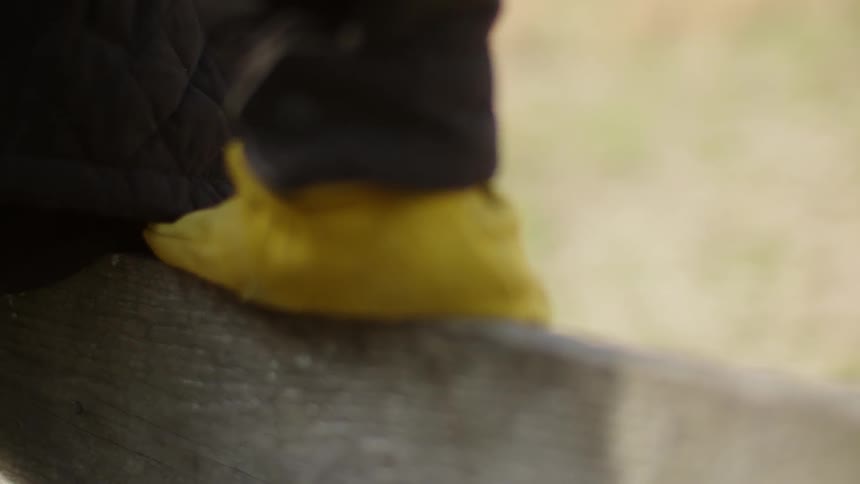 A person is adjusting their hand as they are sitting on a fence in daylight