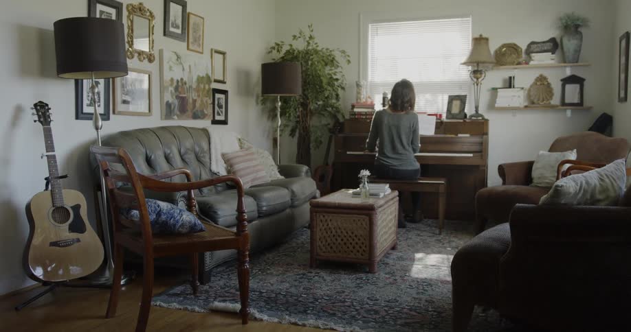 A woman plays a piano in the living room in front of a window