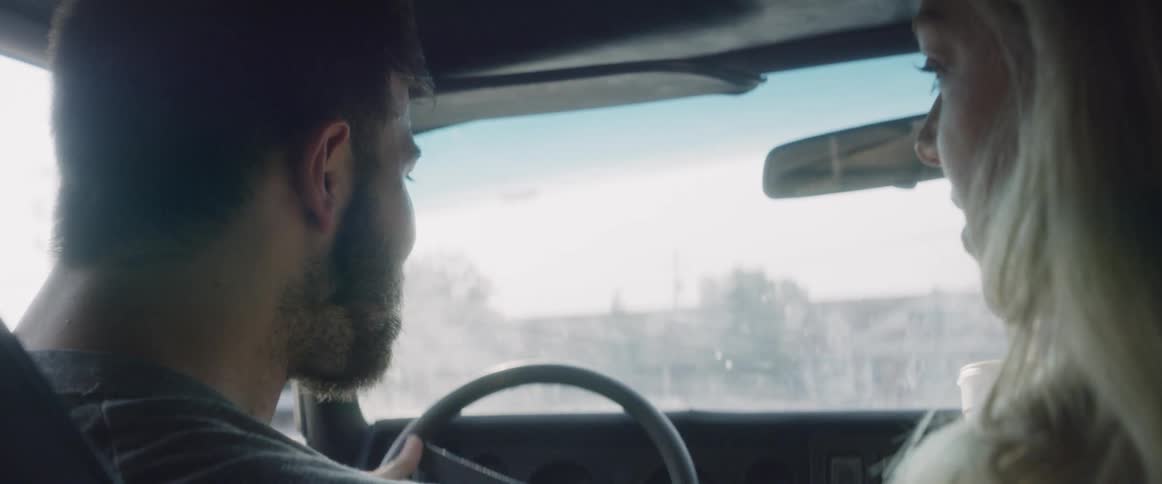 A man and woman are eating and talking while driving on a sunny day