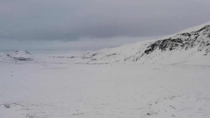 The snow covered field leads to a mountain range on a cloudy day
