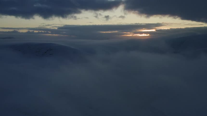 Thick clouds hovering over snowy mountains at sunset
