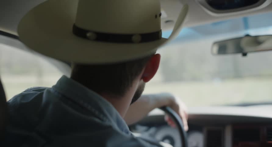 A man in a cowboy hat is driving a car