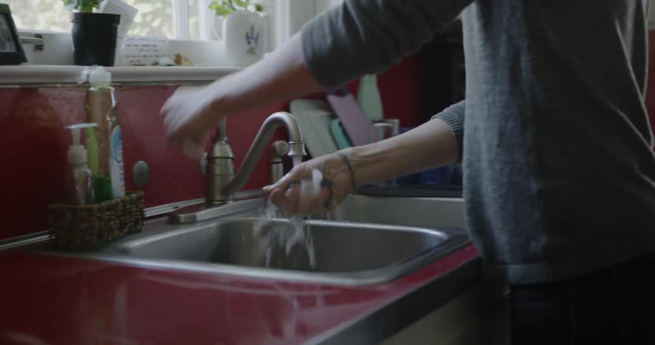 A woman puts soap on the sponge and starts to wash dishes
