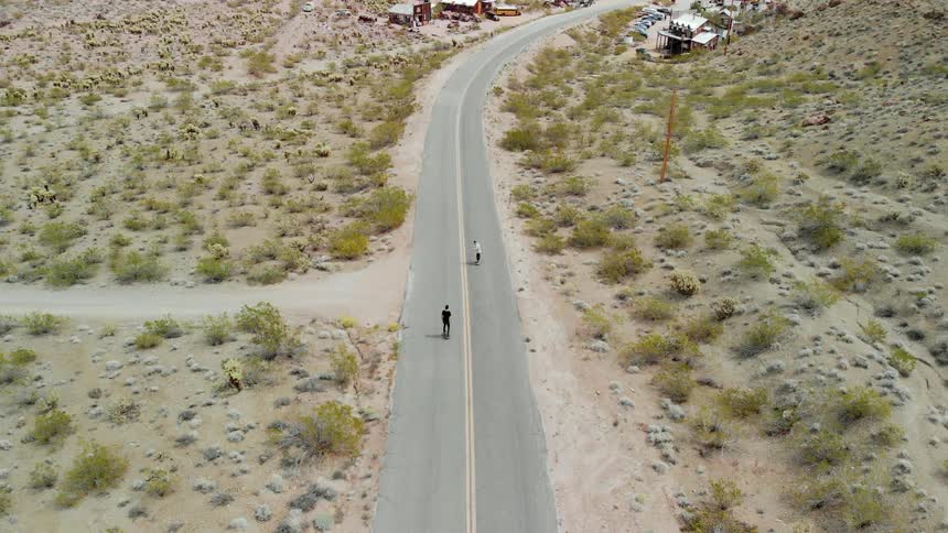 Two men skateboard on a rural road