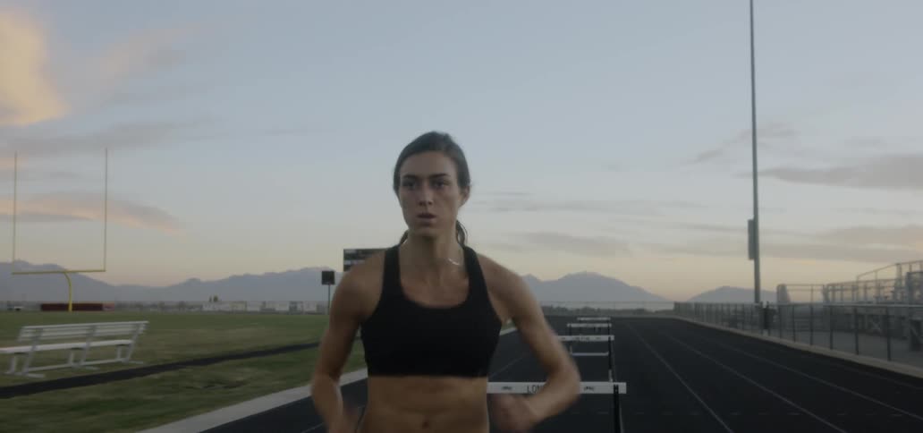 A woman is running and doing hurdles on the track
