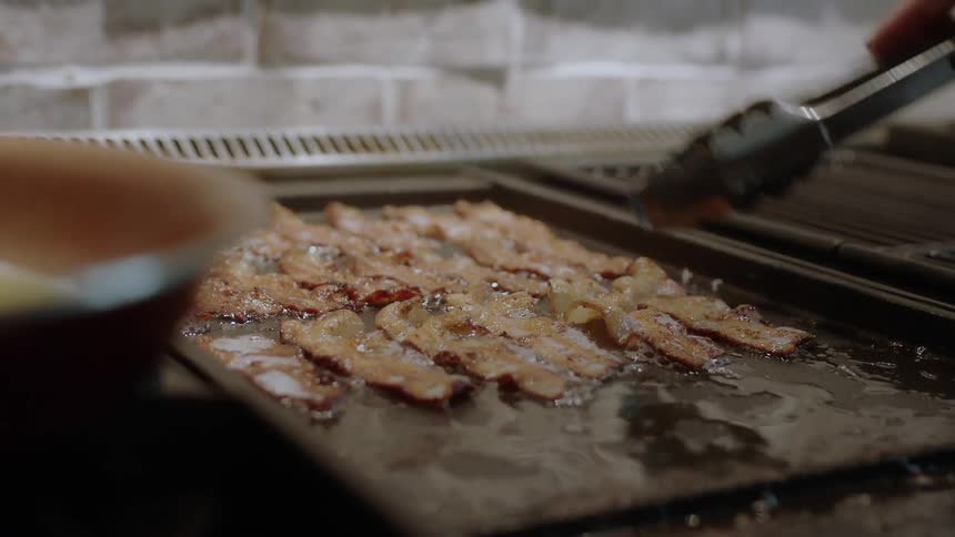 A cook flips bacon as it cooks