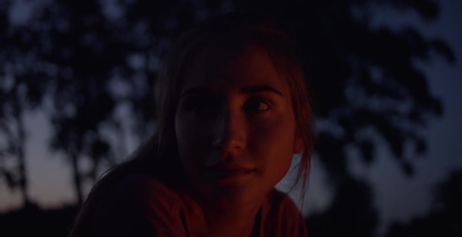 A woman sitting outside at night by a campfire