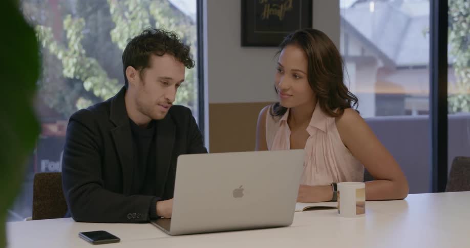 A man and woman talk as they work on a laptop