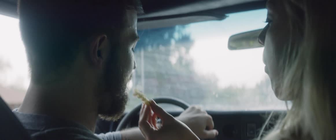 Man drives a car as a woman puts a french fry in his mouth