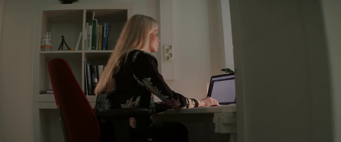 A woman works late at night typing on a laptop at her home desk.