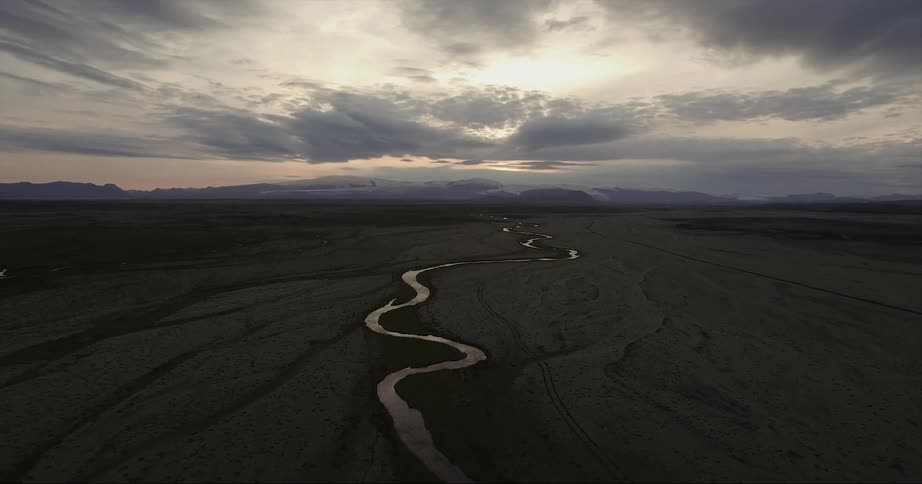 A stream winds through a barren landscape at sunset
