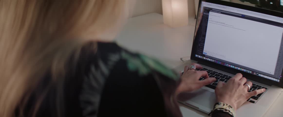 A blonde woman in a patterned top types on her laptop at night