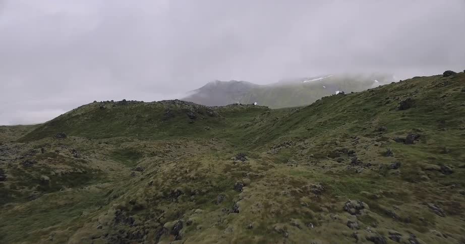 The green hills lead to a fog covered mountain