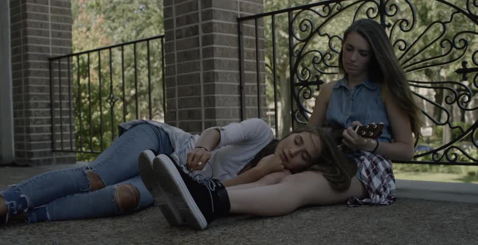 A girl plays guitar as another lays nearby