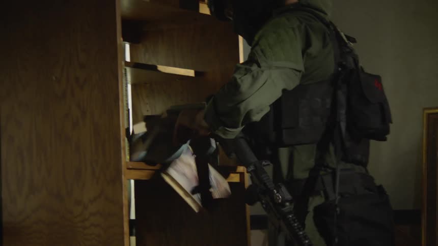 A riot officer searches through a bookcase