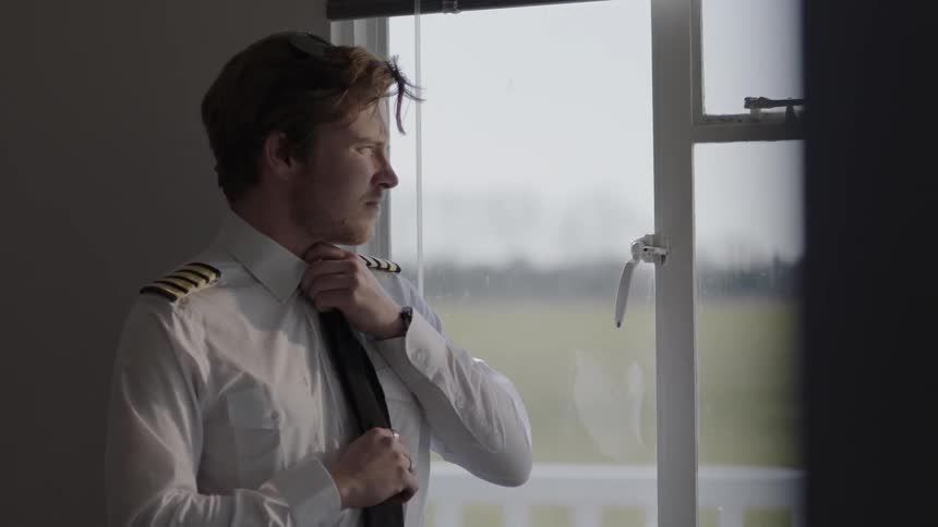 A man tightens his tie by the window