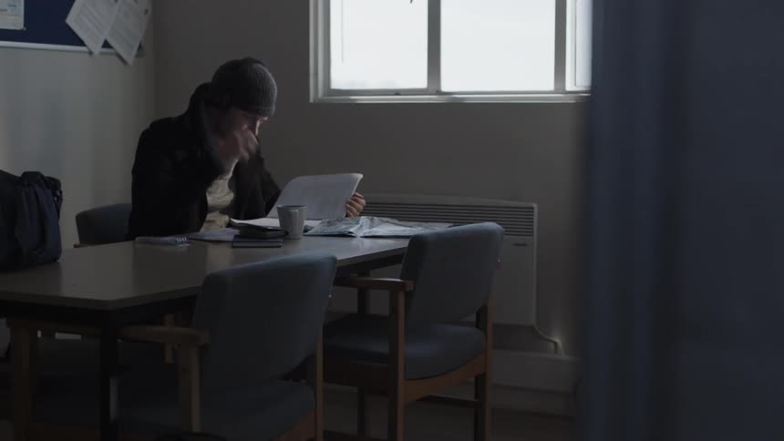 Man sitting at desk wearing headphones is writing in notebook