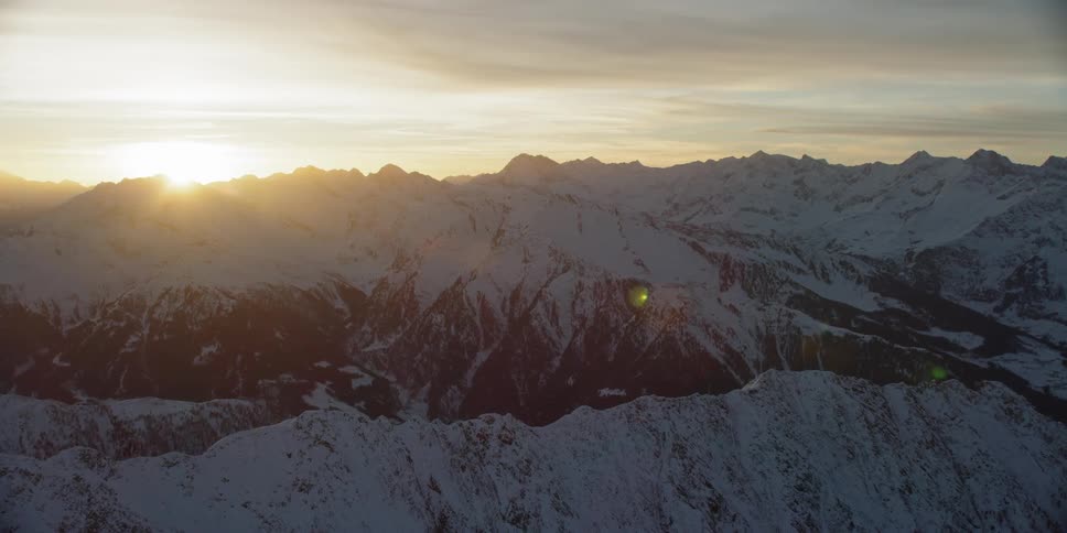 Sun sets behind snow covered mountains