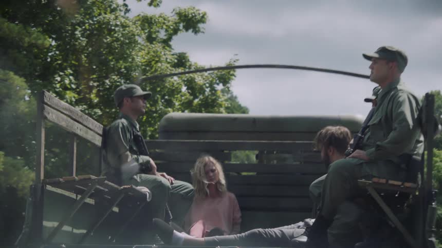 A woman sits in the bed of a truck with several soldiers as it drives off