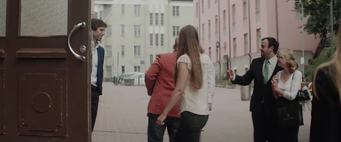People in formal wear talk and enter through an open wooden building door.