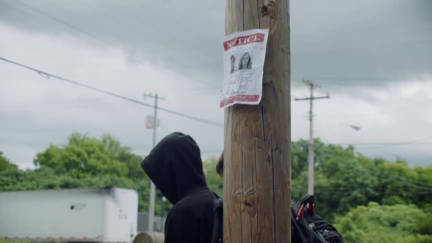 Two teenagers are standing next to a telephone pole with a missing sign on it in daylight