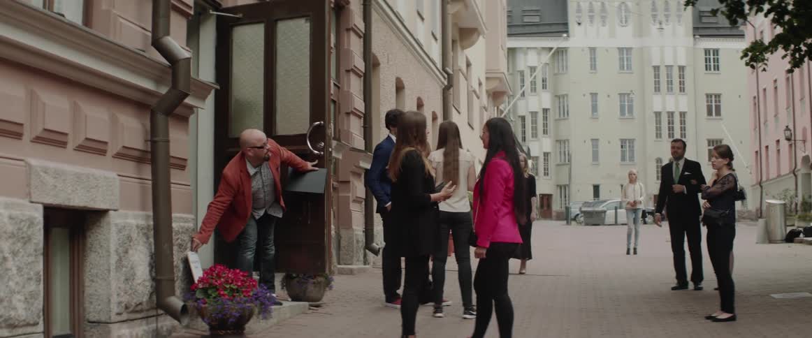 A man is opening a building as a group of people wait outside in daylight