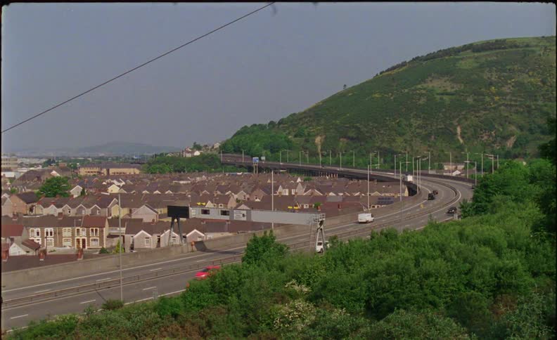 The cars drive around the large road by the homes