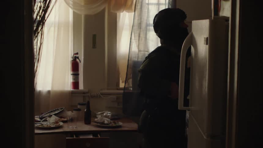A police officer is searching the kitchen cabinets in a house in daylight