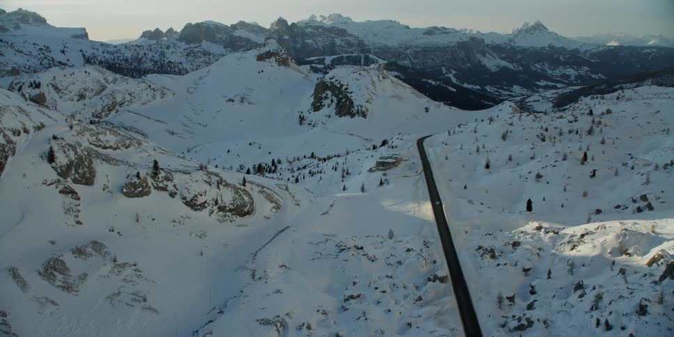 A vehicle travels down the road near the snow covered mountain range