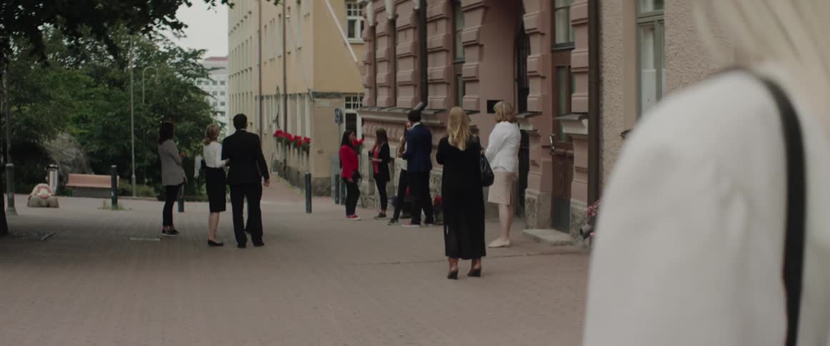 A group of smartly dressed people gathers outside an entrance on a city street.
