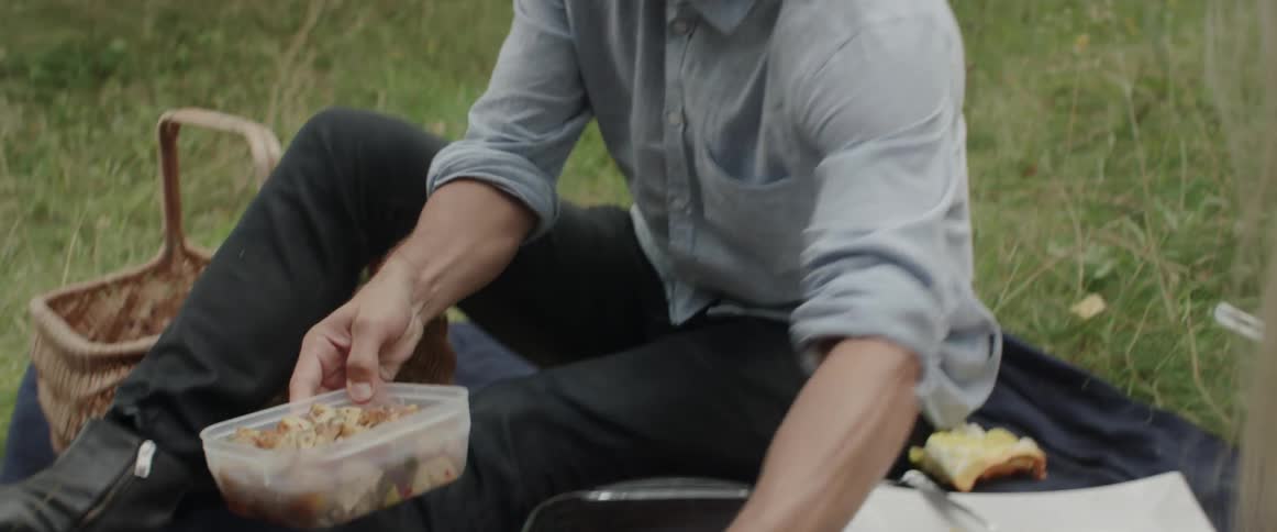 A young man picks up a clear plastic container of food at a picnic.