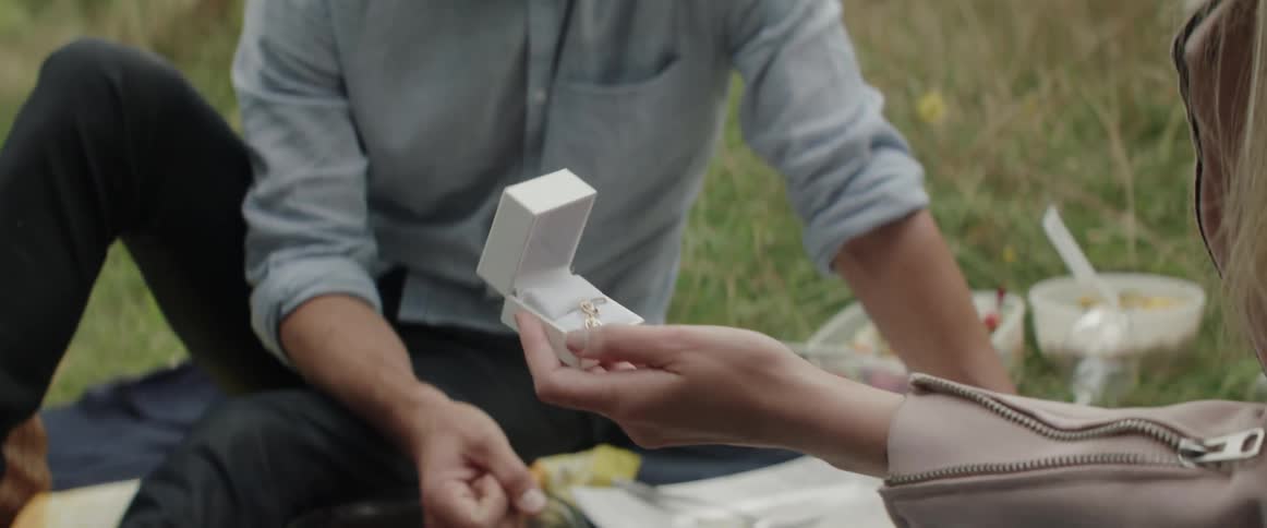 Close up of a man presenting an open ring box during outdoor picnic.
