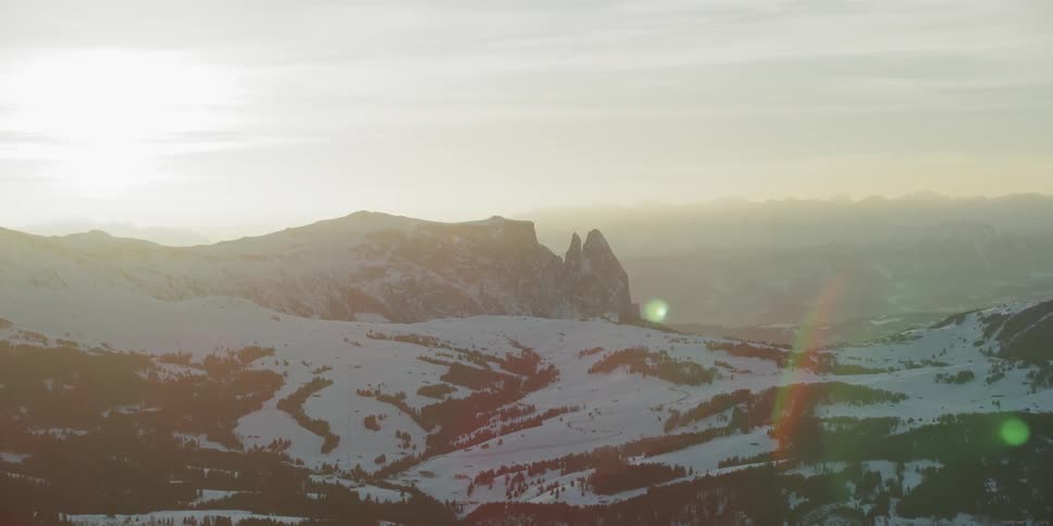 The mountain is covered with trees and snow at sunset