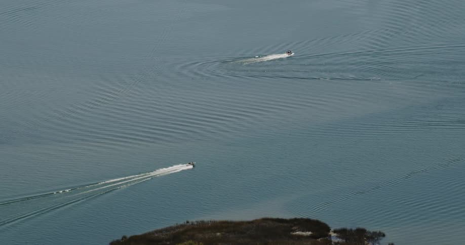 Two boats are speeding off a coastline in daylight