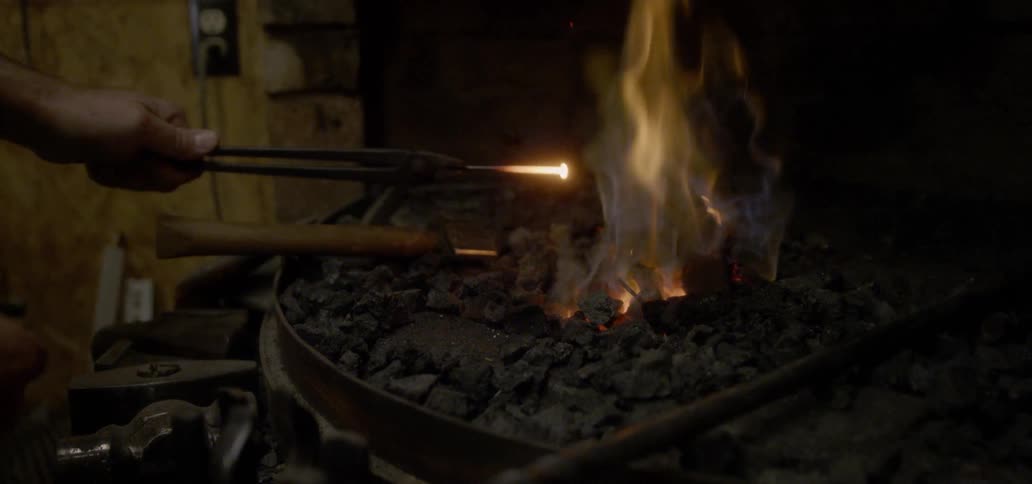 A blacksmith heats a tool in a fire