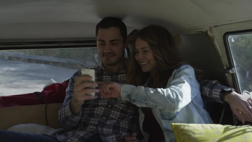 A man and woman laugh and look at a phone in the back of a car