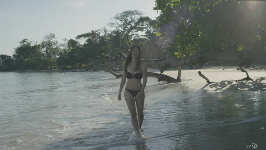 A woman in a bikini wades in the surf and laughs