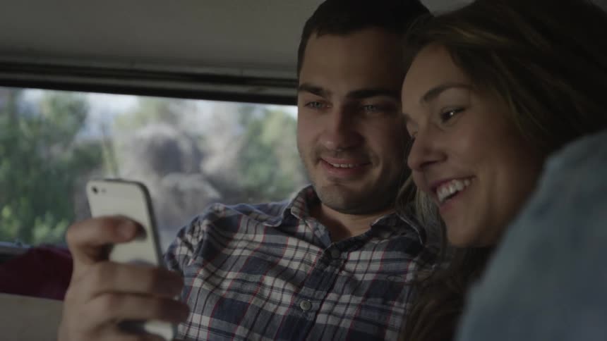 A man and woman laugh as they look at a smartphone