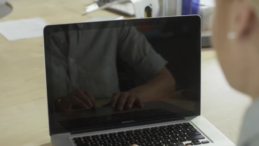 Woman using a laptop and her hands are reflected in the screen