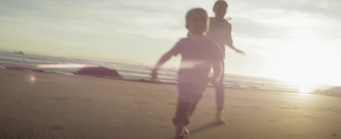 Children run on a beach at sunset