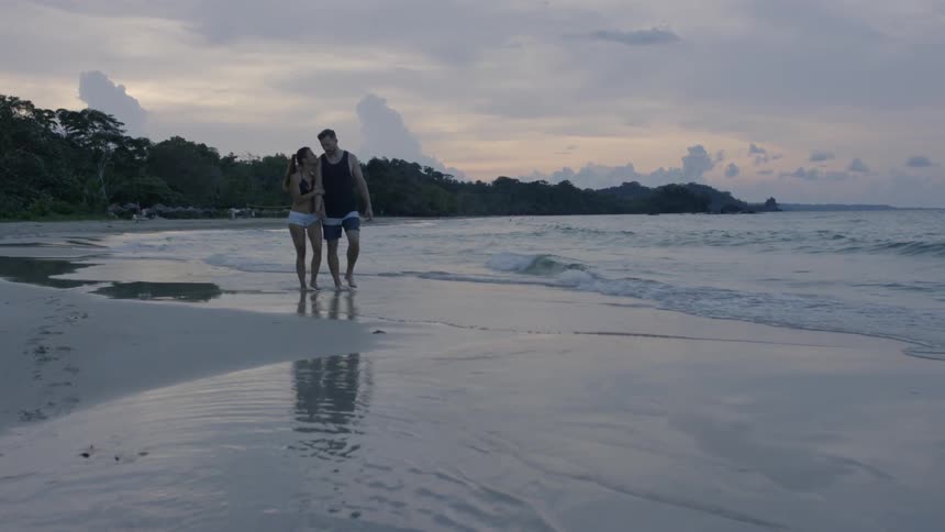 A man and woman hold hands on the beach