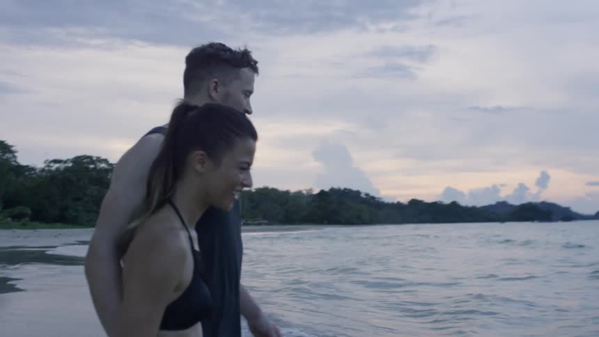 A man walks with a woman into the water of the shore
