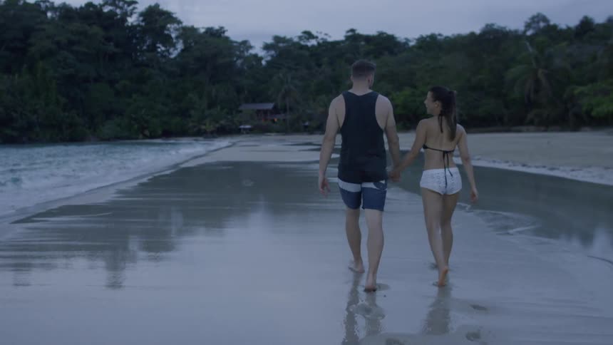 A man and woman hold hands on the beach