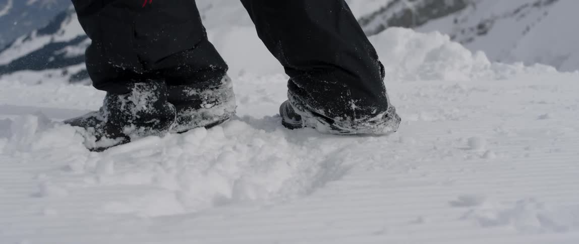 A person is kicking up snow as the land from a jump outside in mountain landscape in daylight