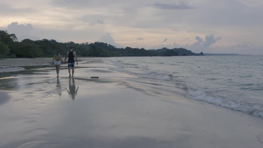 A couple walk hand in hand on the beach