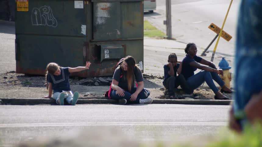 Children sit on the curb across street